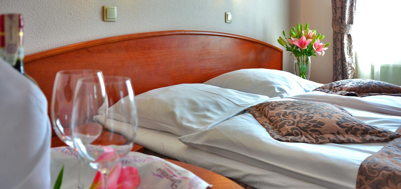 un bel letto matrimoniale in una camera d'albergo, sul comodino un vaso di fiori